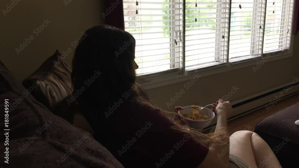 Woman eating steamy noodles from a bowl while on couch watching television. Woman eating steamy noodles from a bowl while on couch watching television.