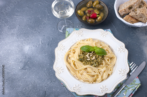 plate with pasta with pesto sauce and olives on a stone background