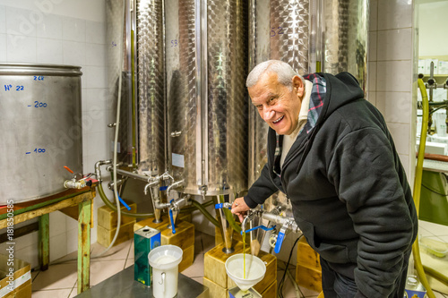 Obraz w ramie old man opens tap of storage silo of olive oil