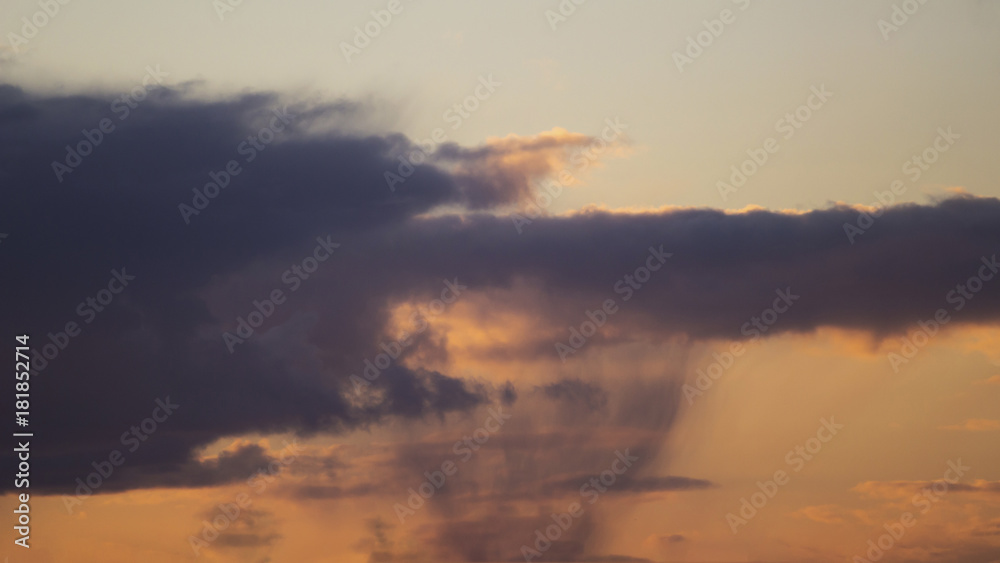 view of a cloud with rain in the distance at sunrise