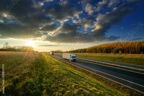 Obraz na płótnie Trucks driving on the highway in autumn landscape at sunset with dramatic clouds w salonie