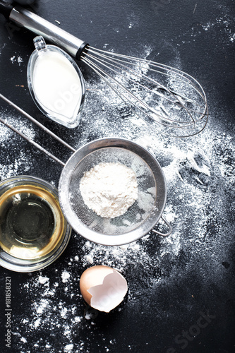 Baking ingredients. Bowl  eggs  flour  eggbeater  rolling pin and eggshells on black chalkboard from above.