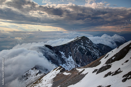 Waterfall like low level orographic clouds flowing down the steep north face of Karavanke Karawanken ridge with snow patches at sunset, Stol Hochstuhl peak Kranjska Slovenia Carinthia Austria Europe