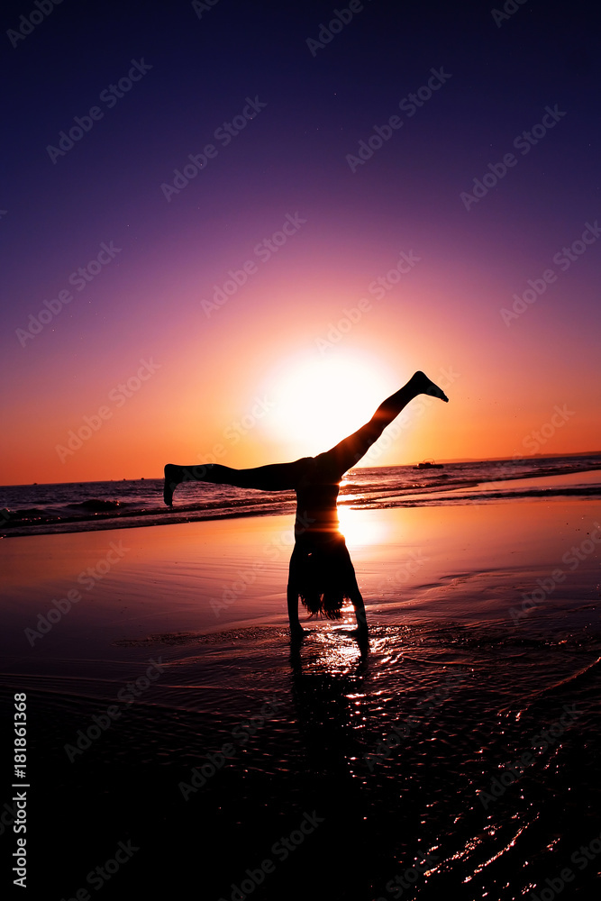 Silhouette of a girl doing a head stand at the beach, in the ocean.