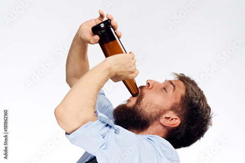 A young guy with a beard on a light background drinks beer