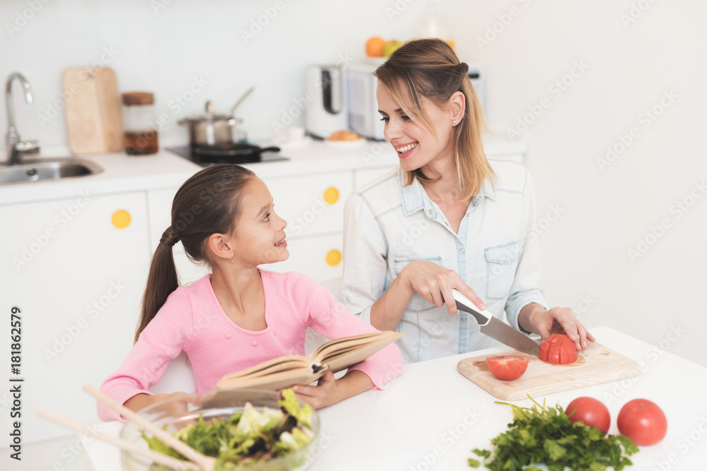 Mom and daughter have fun while preparing a salad. They are in a bright kitchen. Mom and daughter have fun while preparing a salad. They are in a bright kitchen.