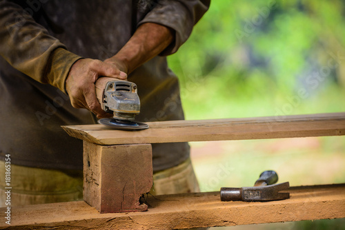 Joiner works with an electric scrubber and processes wooden products.Carpenter with handheld electric scrubber .in the hands on the woodwork.