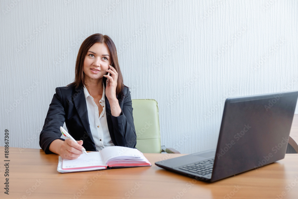 Secretary talking on mobile phone and writing notes while sitting at her desk. Secretary talking on mobile phone and writing notes while sitting at her desk.