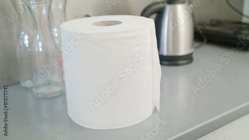 A hand tearing a piece of white paper towel from a roll in the Kitchen. Close-up shot photo