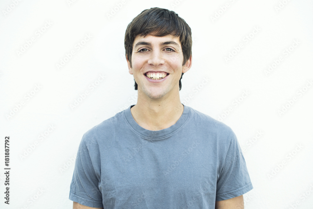 Retrato frontal de hombre con cabello castaño y camiseta gris sobre fondo blanco con expresión de felicidad.