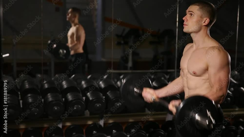 Handsome man with big muscles, posing in the gym muscular man lifting weights over dark background muscular man working out in gym doing exercises with barbell at biceps strong male. close-up Handsome man with big muscles, posing in the gym muscular man lifting weights over dark background muscular man working out in gym doing exercises with barbell at biceps strong male. close-up