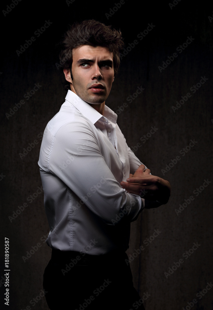 Charismatic sexy male model posing in white style shirt looking serious and energetic on dark shadow background. Closeup portrait.
