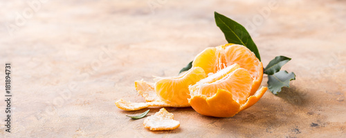 Fresh peeled mandarin with dreen leaves on orange stone background. Healthy food concept with copy space.