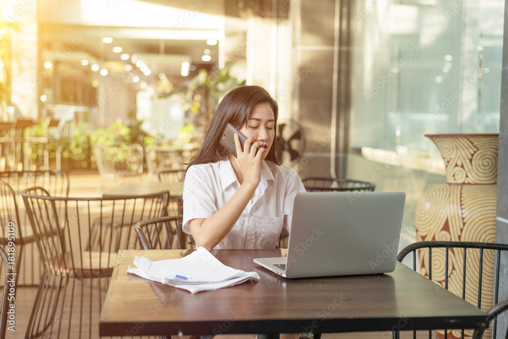 Happy woman talking on phone with customer service and using a laptop sitting in a restaurant Happy woman talking on phone with customer service and using a laptop sitting in a restaurant