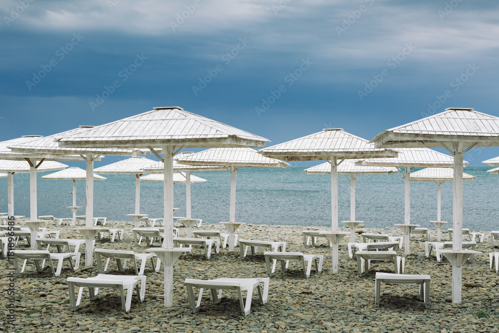 Wooden parasols and empty deckchairs on deserted beach on the off-season cloudy day