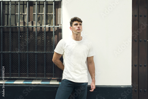 Retrato de hombre joven con camiseta blanca apoyado en la pared de una casa en una calle típica andaluza.