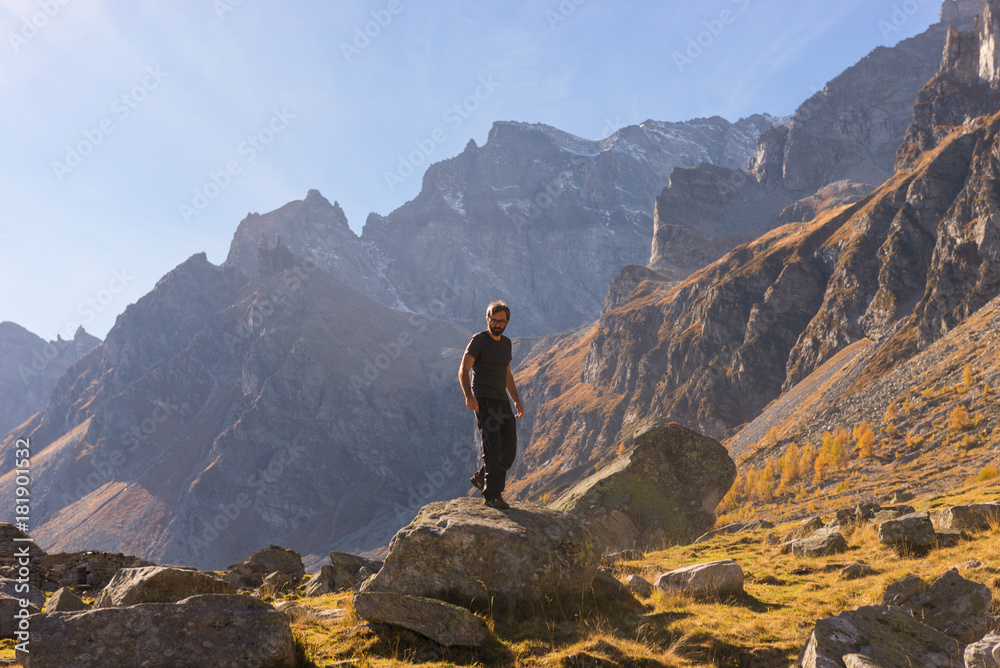 Young adult man hiker climb down a rock on mountain in sunny autumn day on Alps in Italy outdoor.