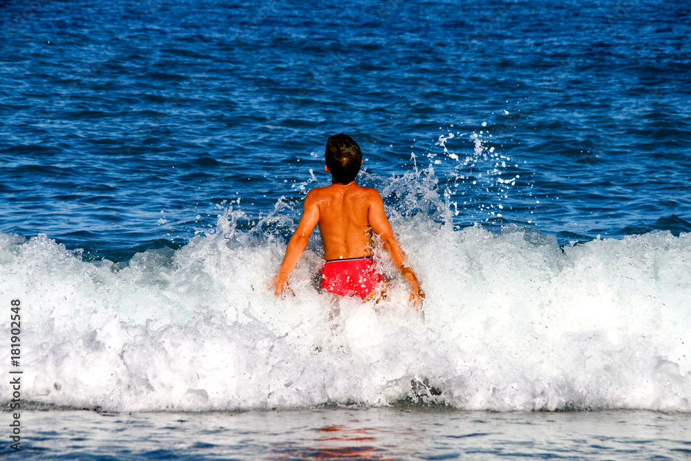 Little sunburnt boy enjoy his Summer vacation in the sea, swimming and play with the waves splashing over him Little sunburnt boy enjoy his Summer vacation in the sea, swimming and play with the waves splashing over him