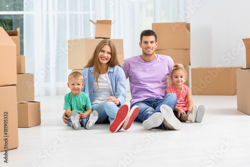 Happy family sitting on floor near moving boxes in their new house