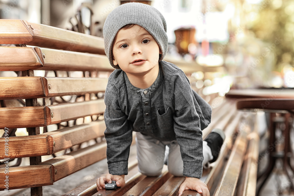 Adorable little boy on bench in outdoor cafe - obrazy, fototapety, plakaty 
