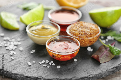 Tableau sur toile Gravy boats with tasty sauces for salad on slate plate