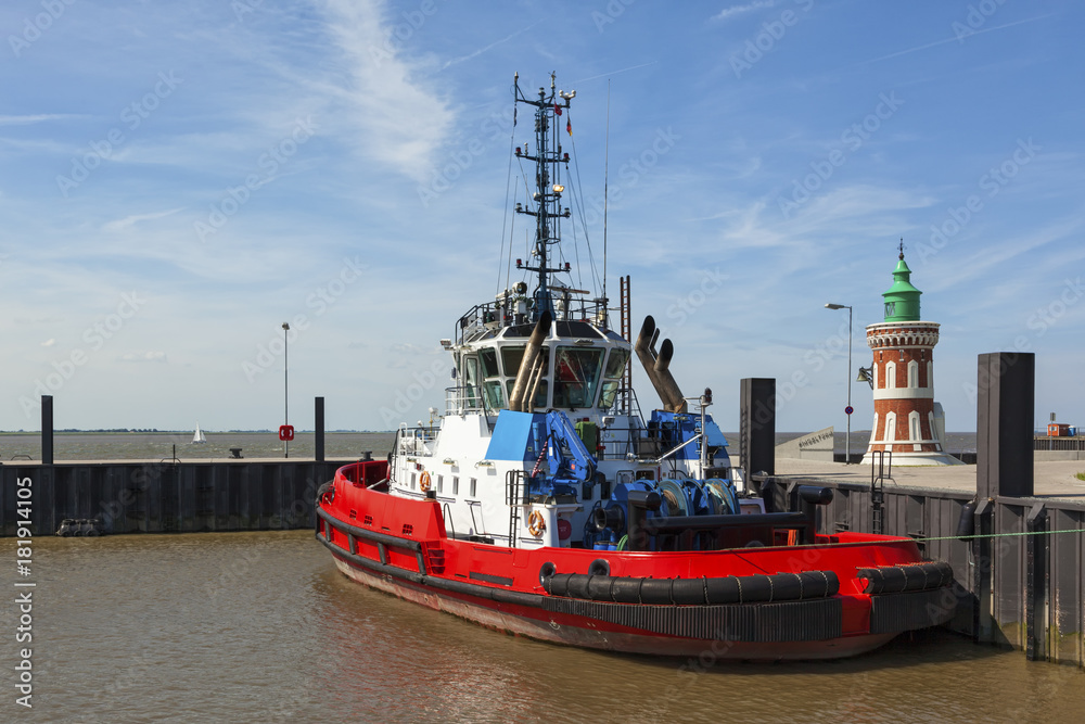 Red tugboat moored next to the historic Pingelturm lighthouse at port of Bremerhaven