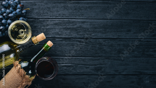 A bottle of wine with glasses and grapes on a black wooden background. Free space for text. Top view.