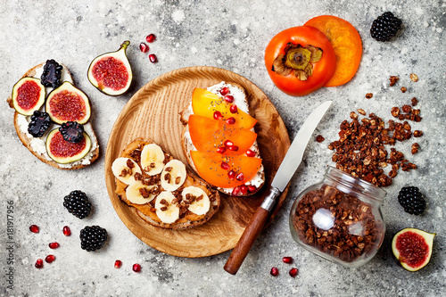 Healthy breakfast toasts with peanut butter, banana, chocolate granola, cream cheese, figs, blackberry, persimmon, pomegranate, chia seeds. Top view, overhead