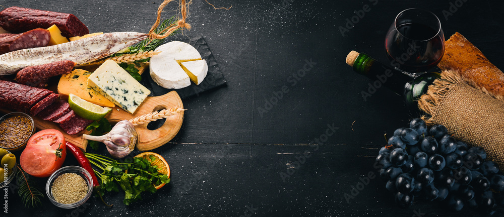 A bottle of wine, cheeses and traditional sausages on a wooden background. Brie cheese, blue cheese, gorgonzola, fuete, salami. Free space for text. Top view. A bottle of wine, cheeses and traditional sausages on a wooden background. Brie cheese, blue cheese, gorgonzola, fuete, salami. Free space for text. Top view.