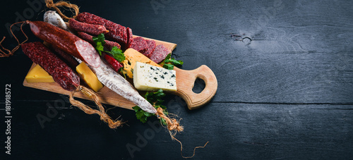 Assortment of cheeses and traditional sausages on a wooden background. Brie cheese, blue cheese, gorgonzola, fuete, salami. Free space for text. Top view.