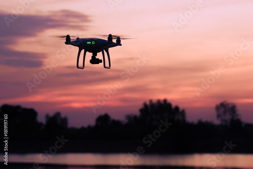Silhouette of modern RC Drone   Quadcopter with camera flying above the river with tree background at sunset