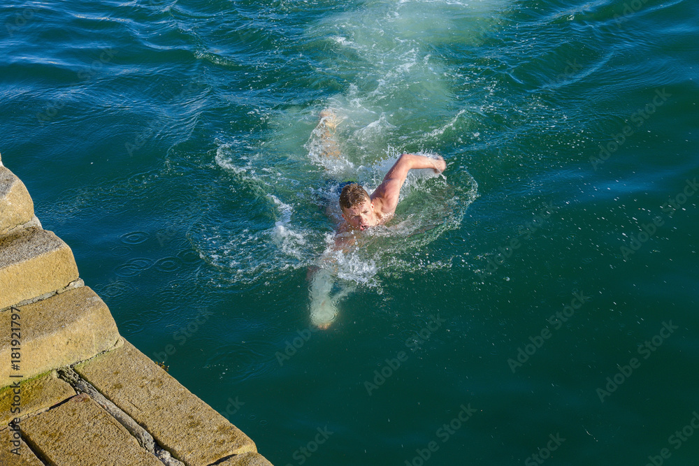 young man swims in the sea near the pier