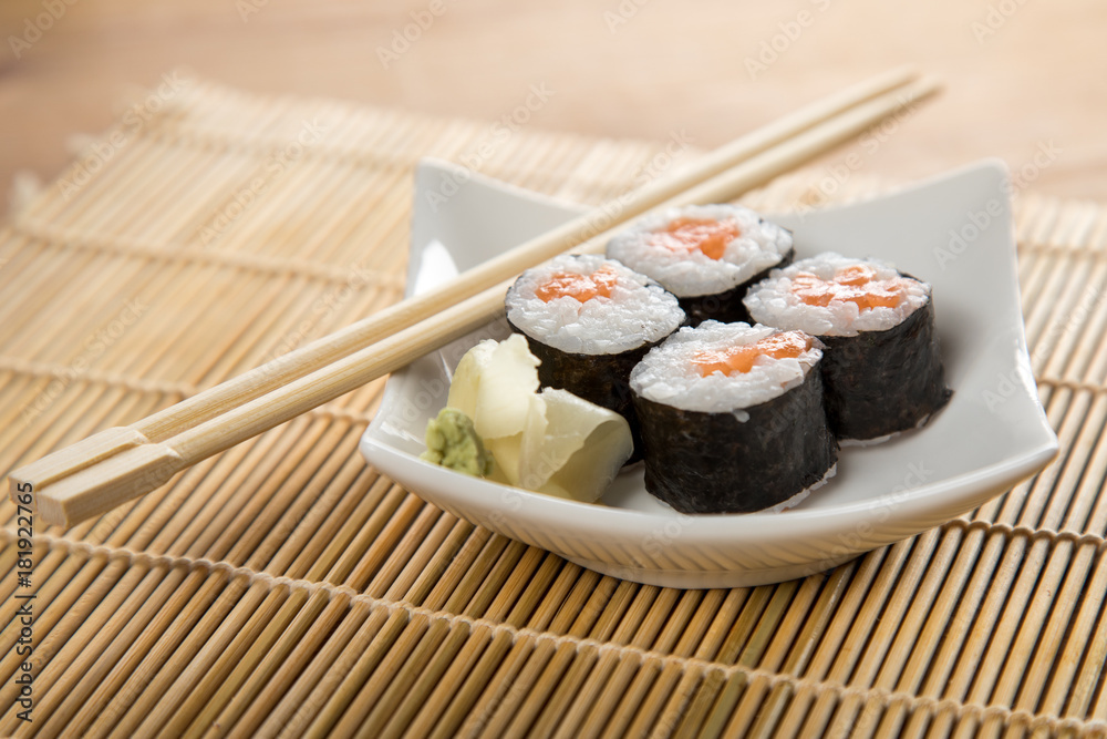 Vier Maki Sushi mit Lachs auf Teller an Holz Stäbchen Vier Maki Sushi mit Lachs auf Teller an Holz Stäbchen