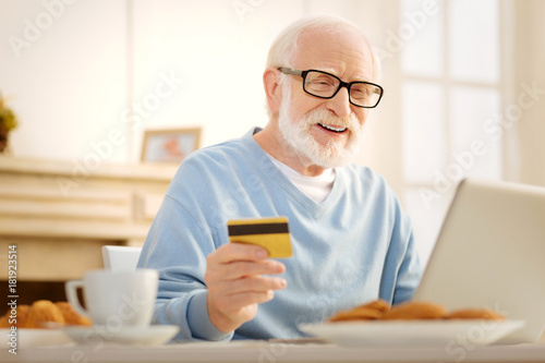 Make me smile. Delighted male person opening mouth and looking downwards while doing online shopping