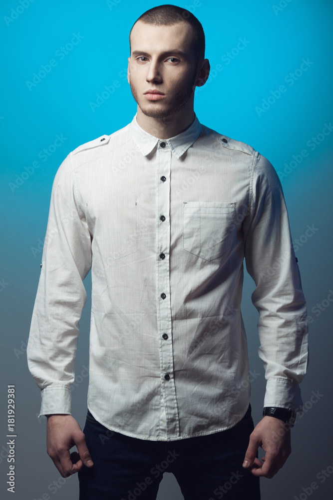 Fototapeta premium Men fashion concept. Portrait of fashionable young man with haircut wearing trendy clothes, posing over blue and gray background. Casual street style. Studio shot