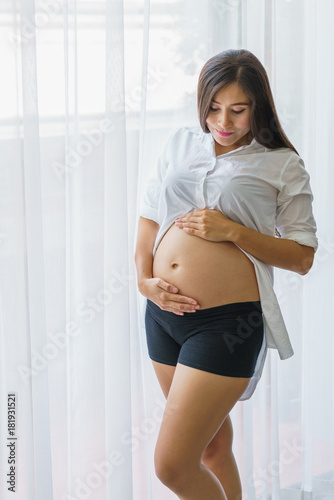 Beautiful pregnant woman standing and hand touch belly at living room. concept of pregnancy, family and lover relation. Free Download Beautiful pregnant woman standing and hand touch belly at living room. concept of pregnancy, family and lover relation. - GFXLoad