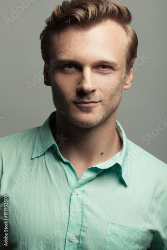 Male beauty, boy next door concept. Portrait of smiling 30-year-old man standing over gray background. Close up. Classic style. Wavy glossy blond hair. Studio shot