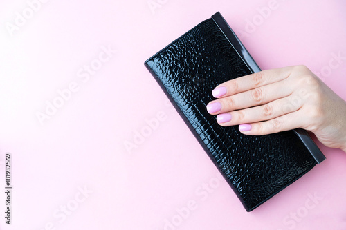 Young woman holding black, leather wallet on pink background. Top view, flat lay. copy space for text. Close up pink nails for girls.