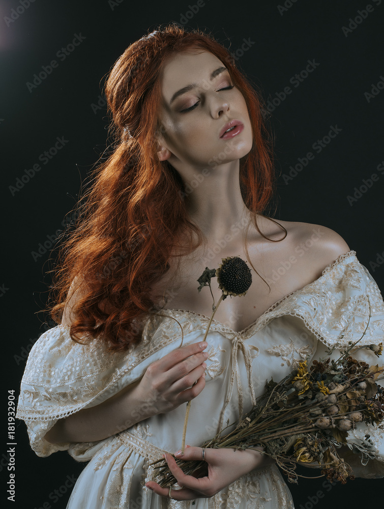 Portrait of a red haired young woman in a vintage gold dress with a dry bouquet in hands on a black background. A princess. Fairy tale. Art photo. Stock Photo Adobe Stock
