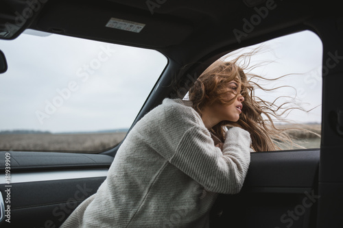 beautiful girl with long windy curly hair looking out from car window