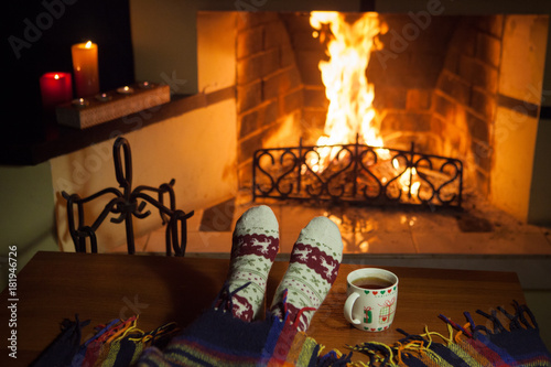 Photos A woman in warm knitted socks with a cup of hot punch in front of the fireplace
