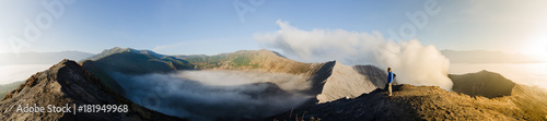 Panorama of Gunung Bromo inner volcano crater  with sulphur fumes and morning mist at sunrise  in Java  Indonesia  with one male adult gazing.