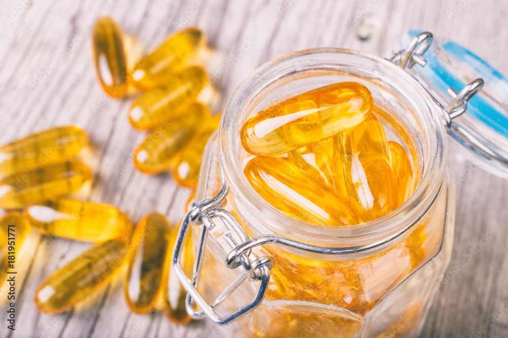 Close up of omega-3 fish fat oil capsules on wooden board in a jar Close up of omega-3 fish fat oil capsules on wooden board in a jar