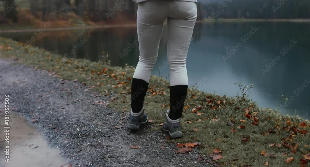 CU TO MED CRANE SHOT Beautiful Caucasian female hiker with backpack walking near beautiful lake in Alps, rainy weather, morning shot. 4K UHD 60 FPS SLO MO CU TO MED CRANE SHOT Beautiful Caucasian female hiker with backpack walking near beautiful lake in Alps, rainy weather, morning shot. 4K UHD 60 FPS SLO MO