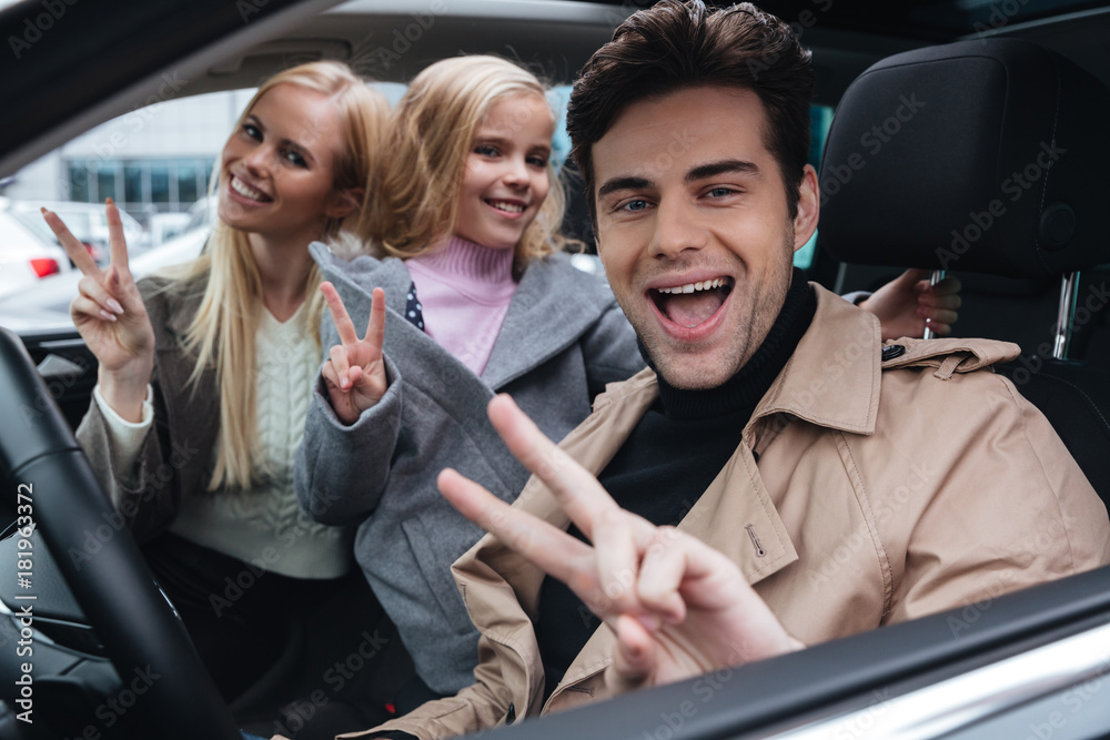 Happy young family sitting in car showing peace gesture