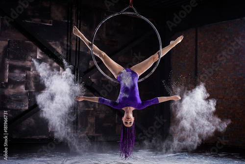 Photos A young, slender girl in a lavender leotard and lilac dreads, doing gymnastics on the air ring, the Hoop and throws the hands of the white powder in the form of a cloud