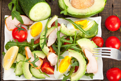 Avocado salad with chicken, rucola and cherry tomatoes in white plate. Horizontal view from above 