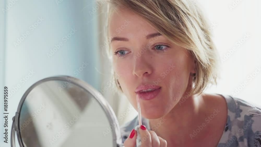 Adult woman makes makeup applying lipstick and looking in the mirror Adult woman makes makeup applying lipstick and looking in the mirror