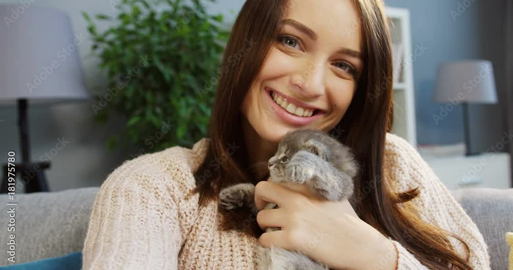 Portrait of a lovely young woman hugging a cute pussycat and smiling into the camera in the cozy room at home. Indoors. Close up Portrait of a lovely young woman hugging a cute pussycat and smiling into the camera in the cozy room at home. Indoors. Close up