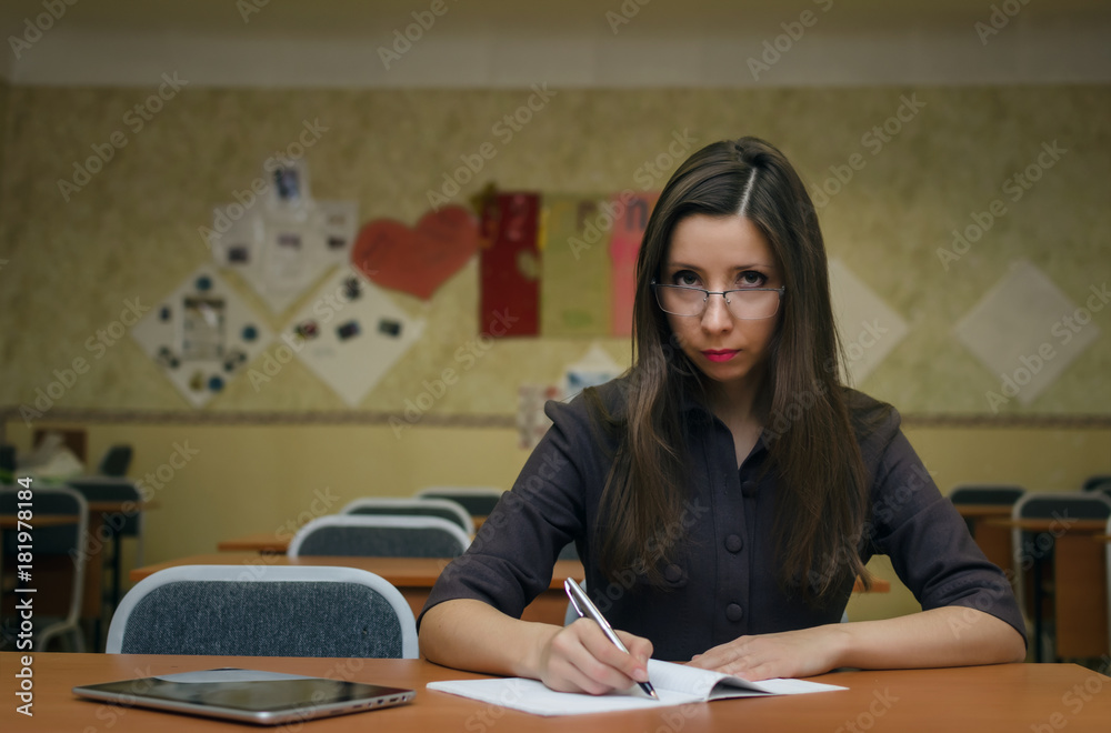 Happy student girl sits at a desk in the class room writes in a notebook and prepares to pass exam. Education concept.